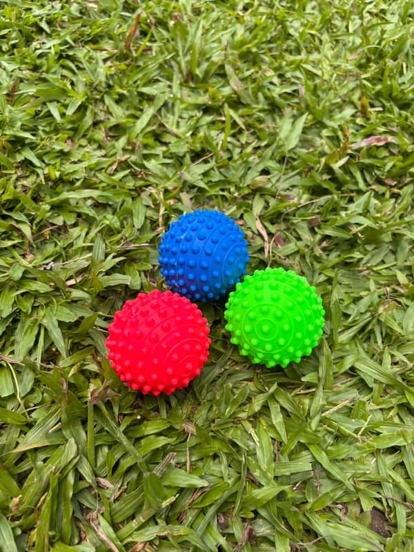 Três bolinhas de borracha com cravos, nas cores azul, vermelha e verde